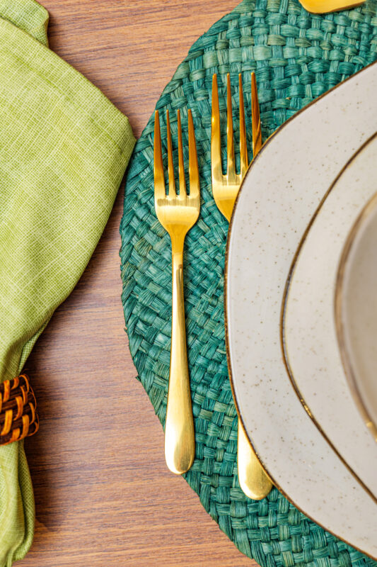 Detalhe de talher dourado sobre sousplat verde com textura em fibra